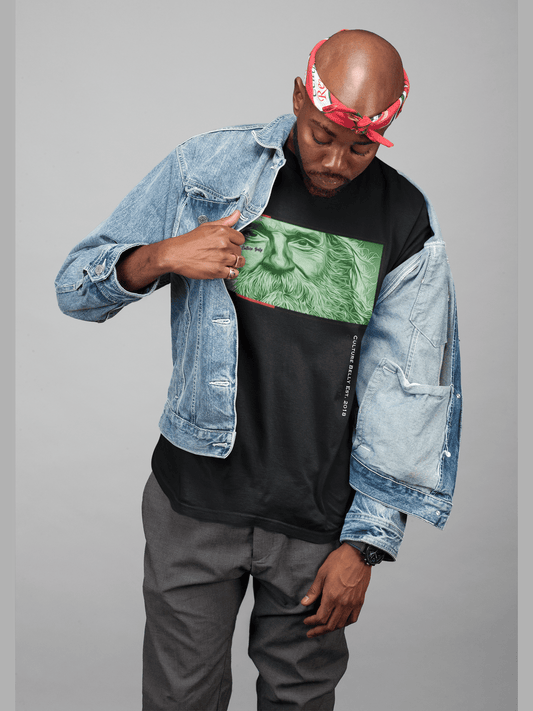 A stylish man with a red bandana and denim jacket reveals a black Culture Belly T-shirt featuring a bold green graphic of a wise, bearded face. The Belly's Forge by Culture Belly.